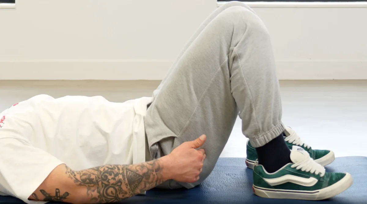 Photogramme d'une vidéo d'exercice OMNEON : un patient allongé sur un tapis, genoux fléchis, réalise un exercice guidé